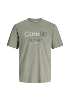 Ελαιόλαδο πράσινο βαμβακερό T-shirt με κοντά μανίκια, που διαθέτει το κείμενο "Core 90" και "Creative Dept." σε αντίθετα χρώματα και διάφορες γραμματοσειρές.