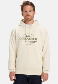Sudadera color crema hecha de una tela suave, con un bolsillo frontal, capucha con cordón y el logo de Quiksilver impreso en verde oliva y marrón.