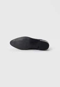 Suola di scarpa in pelle nera con una finitura liscia e texturizzata, dotata di scanalature per la presa e un design della punta affusolato.