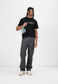 Black t-shirt with "Carhartt" logo, gray cargo pants, cream sneakers, and a light blue crossbody bag. Casual, relaxed fit.