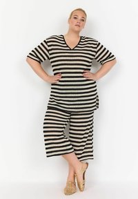 Gestreepte gebreide top met korte mouwen en een V-hals, gecombineerd met bijpassende cropped broeken. Kleuren zijn zwart en crème. Gekocht met beige geweven schoenen.