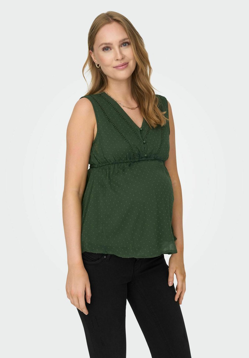 Haut sans manches vert avec un décolleté en V, taille froncé, petit motif à pois et boutons sur le devant, associé à un jean noir.