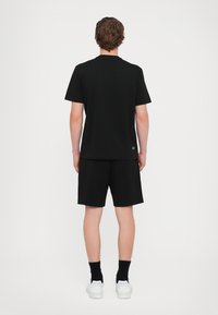 Černé bavlněné tričko s krátkými rukávy a kulatým výstřihem, doplněné černými šortkami. Model nosí bílé tenisky a černé ponožky.