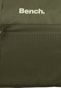 Olijfgroene rugzak met hexagonaal patroon, met een voorvak en een wit logo "Bench." op de bovenkant. Duurzame stoftextuur.