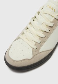 Beige joggesko med teksturert semsket skinn og glatte syntetiske paneler, kremfargede lisser, perforert tå og svart gummisåle. Logo preget i gull.