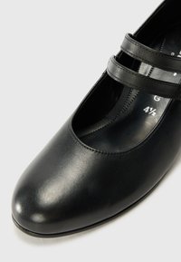 Black leather Mary Jane shoe with a rounded toe, featuring two thin cross straps across the instep and a smooth textured surface.