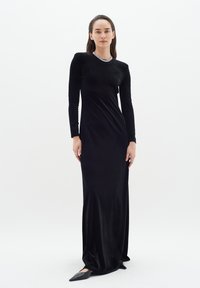 Long black velvet dress with long sleeves and a scoop neck, featuring a sparkling embellishment around the neckline. Fitted silhouette.