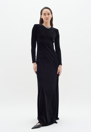 Long black velvet dress with long sleeves and a scoop neck, featuring a sparkling embellishment around the neckline. Fitted silhouette.