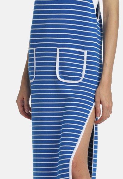 Robe à rayures horizontales bleues et blanches avec deux poches avant et une fente haute sur le côté laissant apparaître la jambe, portée par une personne aux bras nus.