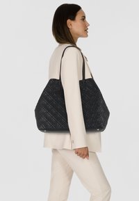 Sac fourre-tout noir matelassé avec un motif floral embossé, des poignées en cuir et une base plate. Ce sac présente un design spacieux et structuré.