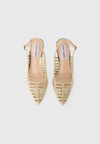 Tacchi slingback dorati con punta affusolata, caratterizzati da cinturini verticali aperti e una fodera interna liscia. Inclusa una cinghia alla caviglia regolabile.