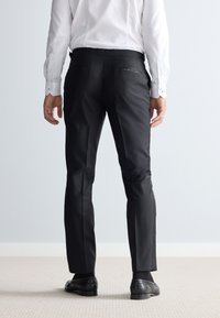 Pantaloni neri da abito con una texture liscia, vestibilità su misura e tasche posteriori. Abbinati a una camicia bianca e scarpe nere.