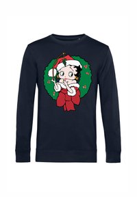Námořnický modrý svetr s potiskem kreslené postavičky v santovském oblečení, obklopené zeleným věncem s červenými detaily a mašlí.