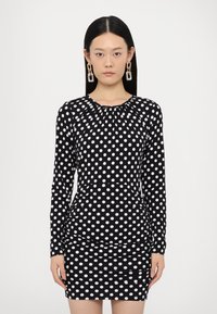 Black dress with white polka dots, long sleeves, gathered neckline, and fitted silhouette, featuring a ruched skirt detail.