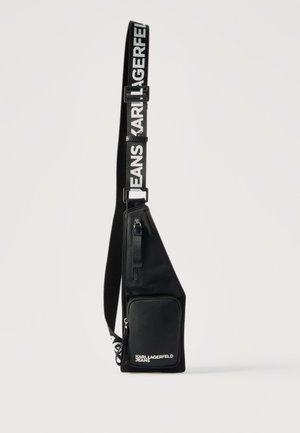 Fekete keresztpántos válltáska elöl cipzáras zsebbel és állítható pánttal, amelyen fehér betűkkel a "KARL LAGERFELD JEANS" felirat olvasható.