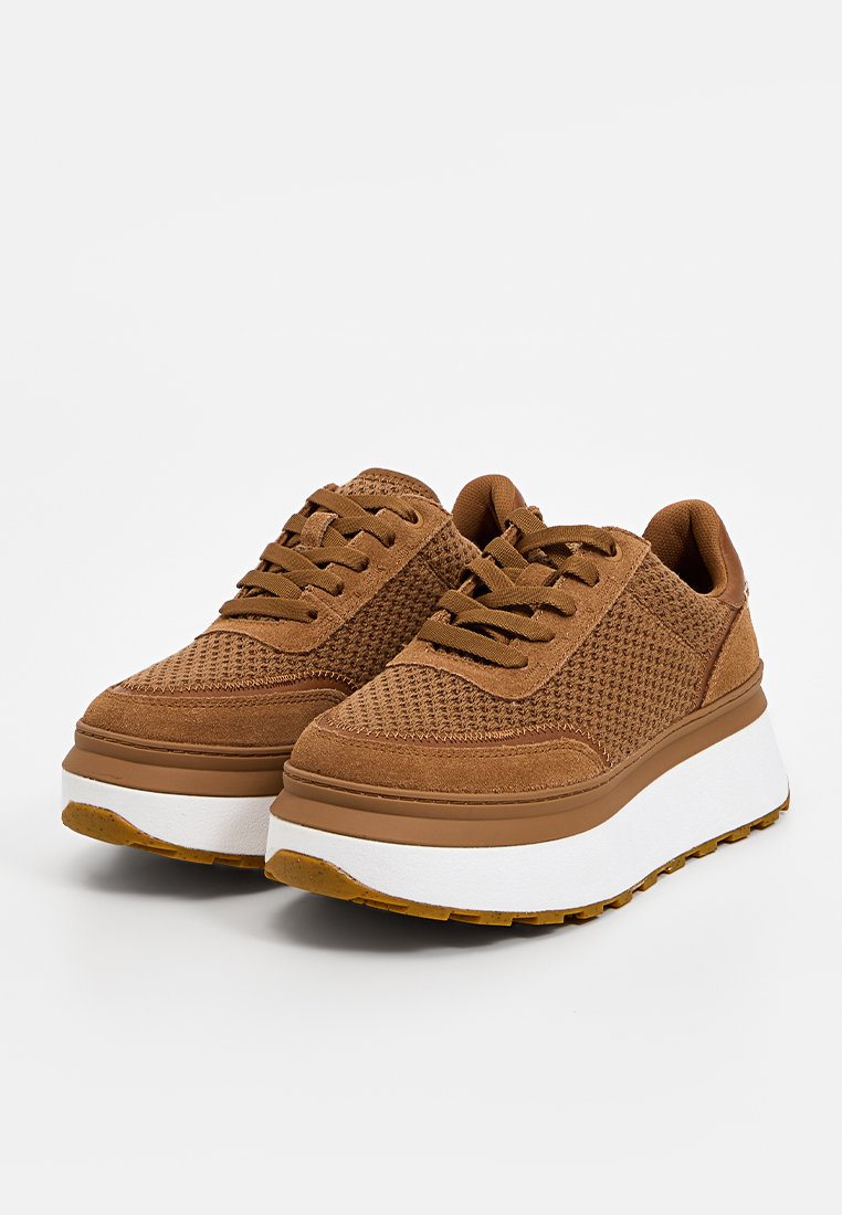 Braune Wildleder- und Mesh-Sneaker mit einem strukturierten Obermaterial, flachen Schnürsenkeln und einer dicken weißen Sohle. Die Außensohle hat ein gemustertes Profil für besseren Halt.