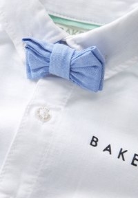 Biela košeľa s svetlomodrou textúrovanou kravatu, ktorá má okrúhly strieborný logový gombík s nápisom "BAKER BY TED BAKER."
