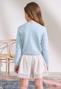 Light blue cropped sweater with long sleeves, paired with white, textured shorts featuring a decorative lace trim at the hem.