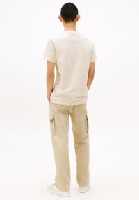 Beige cotton t-shirt and light khaki cargo pants with side pockets, paired with white sneakers. Simple, casual design.