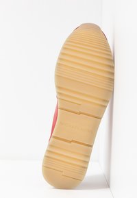 Baskets rouges avec une semelle en caoutchouc texturée et un motif rainuré. Présentent l'inscription "MICHAEL KORS" en relief sur la semelle extérieure. Design minimaliste.