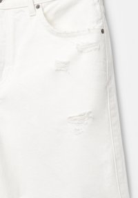 White denim jeans featuring distressed details, with frayed patches and visible stitching. Five-pocket design with metal hardware accents.