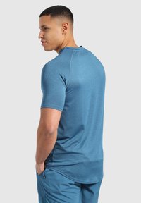 Męska dopasowana koszulka sportowa z krótkim rękawem, wykonana z teksturowanej, heatherowej tkaniny w odcieniu niebieskim, z okrągłym dekoltem i dłuższym tyłem dla lepszej osłony.