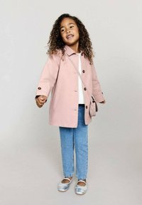 Vaaleanpunainen puuvillatakki napitusyksityiskohdilla, valkoinen paita, siniset farkut ja hopeiset ballerinat, asusteena pieni olkalaukku.