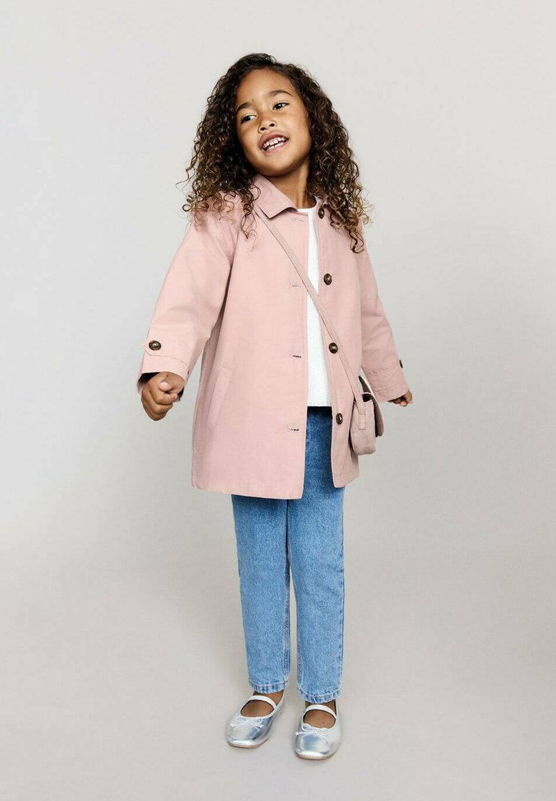 Vaaleanpunainen puuvillatakki napitusyksityiskohdilla, valkoinen paita, siniset farkut ja hopeiset ballerinat, asusteena pieni olkalaukku.