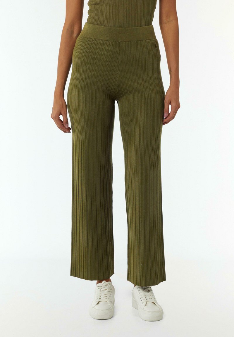 Olijfgroene ribgebreide wijde broek met hoge taille en textuurdetails; gedragen met witte sneakers.