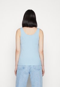 Light blue ribbed tank top with a scoop neckline, fitted design, and wide shoulder straps, paired with high-waisted light blue jeans.