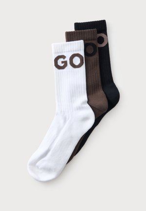 Trois paires de chaussettes côtelées montantes en blanc, marron et noir, chacune avec les lettres "GO" tricotées près du haut.