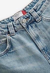Lichtblauwe denim jeans met een middelhoge taille, voorzien van oranje stiksels, een metalen knoopsluiting en voorzakken. Het label zegt "Barrel."