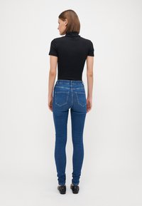 Black ribbed short-sleeve top paired with blue skinny jeans. The jeans feature five pockets and a classic denim texture.