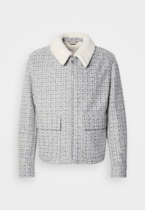 Světle šedý kostkovaný kabát se zipem v přední části, dvěma klopovými kapsami a bílým chlupatým límcem, vystavený na jednoduchém pozadí.