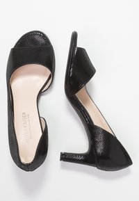 Para czarnych sandałów na obcasie z odkrytymi palcami, z teksturowanymi paskami i niskimi obcasami typu kitten heels, wyeksponowanych na białym tle.
