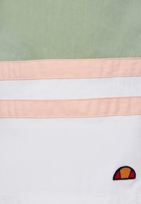 Camisa de manga corta con bloques de color que presenta secciones en verde, rosa y blanco. Incluye un pequeño logo bordado en naranja y rojo.