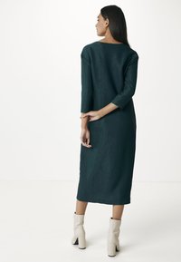 Ciemnozielona sukienka midi o luźnym kroju, z rękawami 3/4 i prostym dołem. Noszona z białymi botkami za kostkę oraz fakturowanym materiałem.