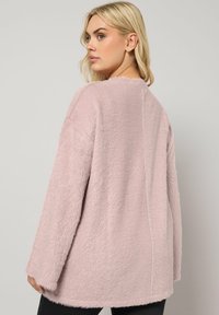 Veste rose en fourrure avec une coupe décontractée, des manches longues et un ourlet droit. Le tissu a une texture douce et un design simple et épuré.