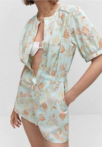 Kwiatowy kombinezon w jasnoniebieskim materiale z bufkami, głębokim dekoltem w kształcie V i elastycznym pasem. Udekorowany pomarańczowymi i różowymi kwiatami.