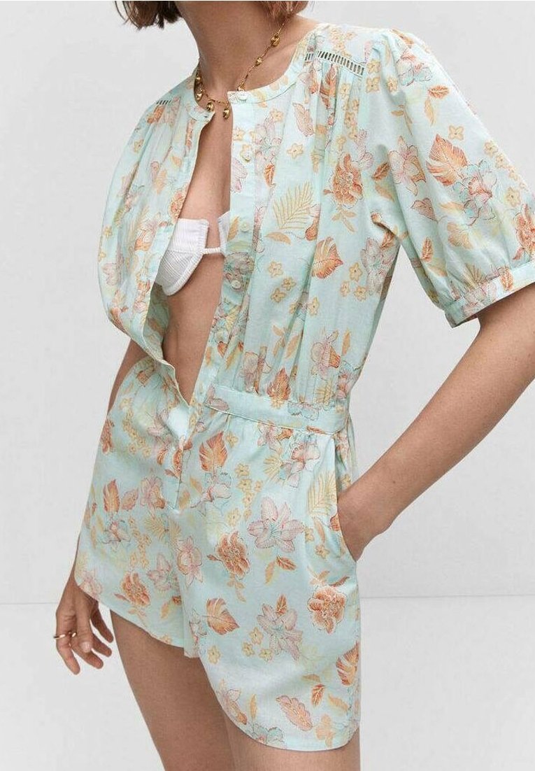 Kwiatowy kombinezon w jasnoniebieskim materiale z bufkami, głębokim dekoltem w kształcie V i elastycznym pasem. Udekorowany pomarańczowymi i różowymi kwiatami.