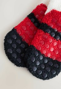 Røde og sorte fuzzy sokker med teksturerede gummigripprikker på sålerne, der har en blanding af bløde og glatte overflader.