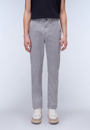 Grijze, toelopende chinos van een gladde stof, met knoopsluiting en steekzakken, gecombineerd met lichtgekleurde sneakers met beige accenten.