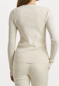 Ribbad krämfärgad långärmad topp med rundad hals, figurnära passform och en subtil textur, tillsammans med matchande ljusa byxor.