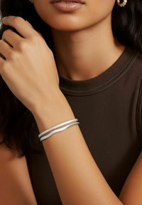 Bracciale d'argento con due fili ondulati, superficie texturizzata, indossato su un avambraccio; sullo sfondo è visibile un indumento scuro e aderente.