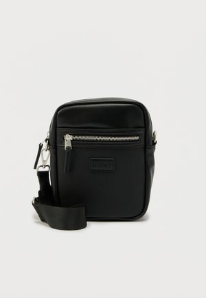 Small black crossbody bag with front zip pocket, adjustable strap, and rectangular shape against plain white background.