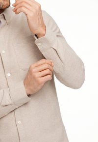 Camicia beige in cotone con colletto button-down, maniche lunghe e taschino sul petto. Il tessuto ha una finitura leggermente testurizzata.