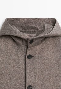 Camicia di lana marrone con colletto piegato, quattro bottoni neri e una finitura morbida e testurizzata. Il tessuto presenta un motivo sfumato sottile.