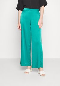 Teal vide bukser i et glat, lette stof, med høj talje og afslappet pasform. Kombineret med hvide block-heeled sandaler.