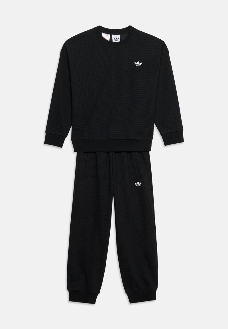 Μαύρη φόρμα Adidas με μακριά μανίκια και παντελόνι, με λευκά λογότυπα Adidas Trefoil στο στήθος και στον αριστερό μηρό.