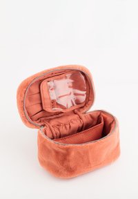 Koralowe pluszowe etui na kosmetyki z zamkiem błyskawicznym, przezroczystą kieszenią, elastycznymi paskami i siatkową przegrodą, o miękkiej fakturze i okrągłym kształcie.